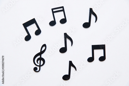 Top view photograph of six black paper cutout music notes on a solid white background. The music notes include two quarter notes, two eighth notes, one treble clef, and one whole note, each cut precis