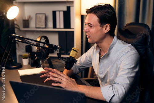 Host channel smart broadcaster talking on live social media application searching on laptop, broadcasting streamer wearing headphone using mic at modern home office studio in warm lighting. Pecuniary.
