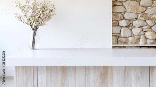 A white countertop displays a glass vase holding delicate white flowers. A stone wall is partially visible in the background. The image is sharp, well-lit, and features a minimalist aesthetic with so