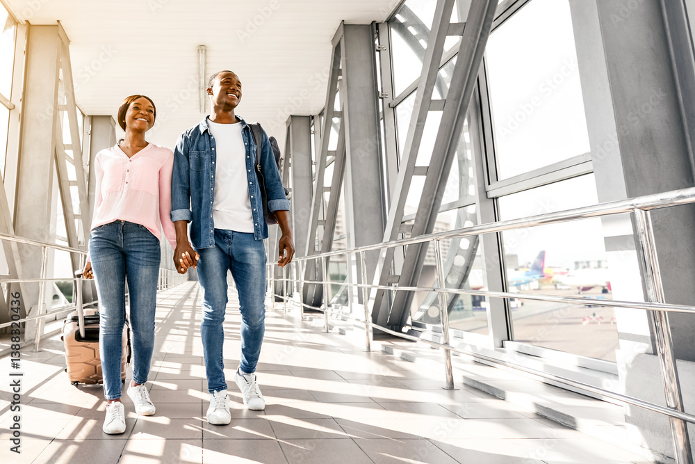 Fototapeta premium Travelling Together. Cheerful Black Couple Holding Hands While Walking In Airport Terminal, Happy African American Spouses Carrying Luggage Suitcases While Going To Boarding Gate, Copy Space