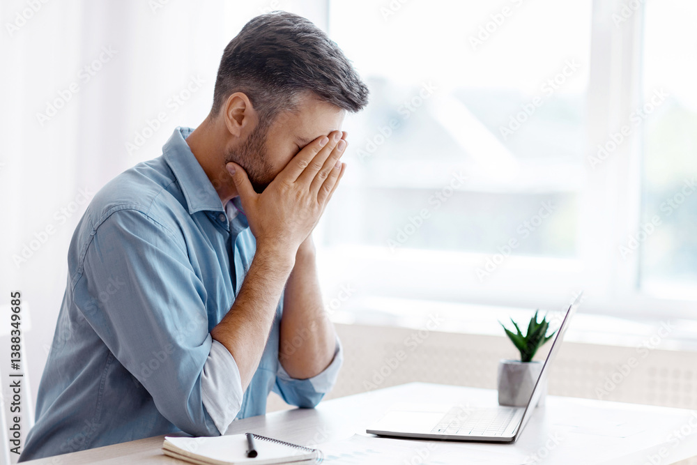 Remote Work Stress. Tired freelancer man sitting at desk with laptop at home office, overworked man covering face with hands, feeling fatigue and lack of inspiration, having problems with project Remote Work Stress. Tired freelancer man sitting at desk with laptop at home office, overworked man covering face with hands, feeling fatigue and lack of inspiration, having problems with project