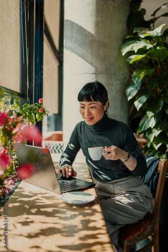 Quadro su tela Asian freelancer woman working remotely from coffee shop using laptop and drinki