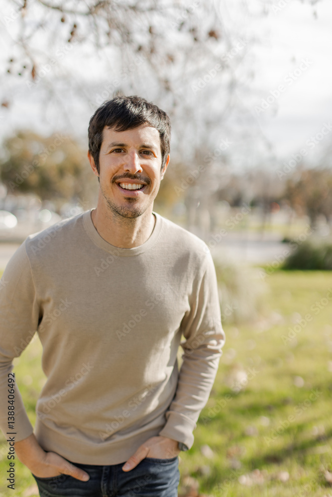 Close-up of cheerful man outdoors on a sunny day, hands in pockets, looking at camera and a friendly smile. Self-confidence, friendliness, lifestyle or wellness concepts. Vertical, natural setting. Close-up of cheerful man outdoors on a sunny day, hands in pockets, looking at camera and a friendly smile. Self-confidence, friendliness, lifestyle or wellness concepts. Vertical, natural setting.
