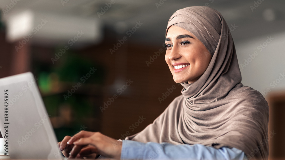 Cheerful arab lady in hijab working online at cafe, using laptop, copy space. Side view of smiling muslim woman freelancer typing on laptop, enjoying her new distant job, chatting with clients Cheerful arab lady in hijab working online at cafe, using laptop, copy space. Side view of smiling muslim woman freelancer typing on laptop, enjoying her new distant job, chatting with clients
