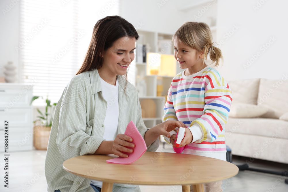 Cute little girl helping her mother wiping wooden table at home Cute little girl helping her mother wiping wooden table at home