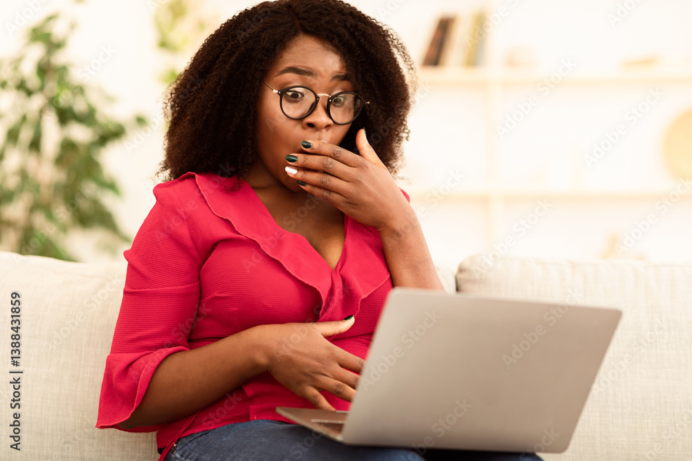 Fototapeta premium No Way, I Can't Believe. Portrait ot surprised african american lady in glasses covering mouth in amazement, reading unexpected news on laptop computer, sitting on the couch at home, copy space