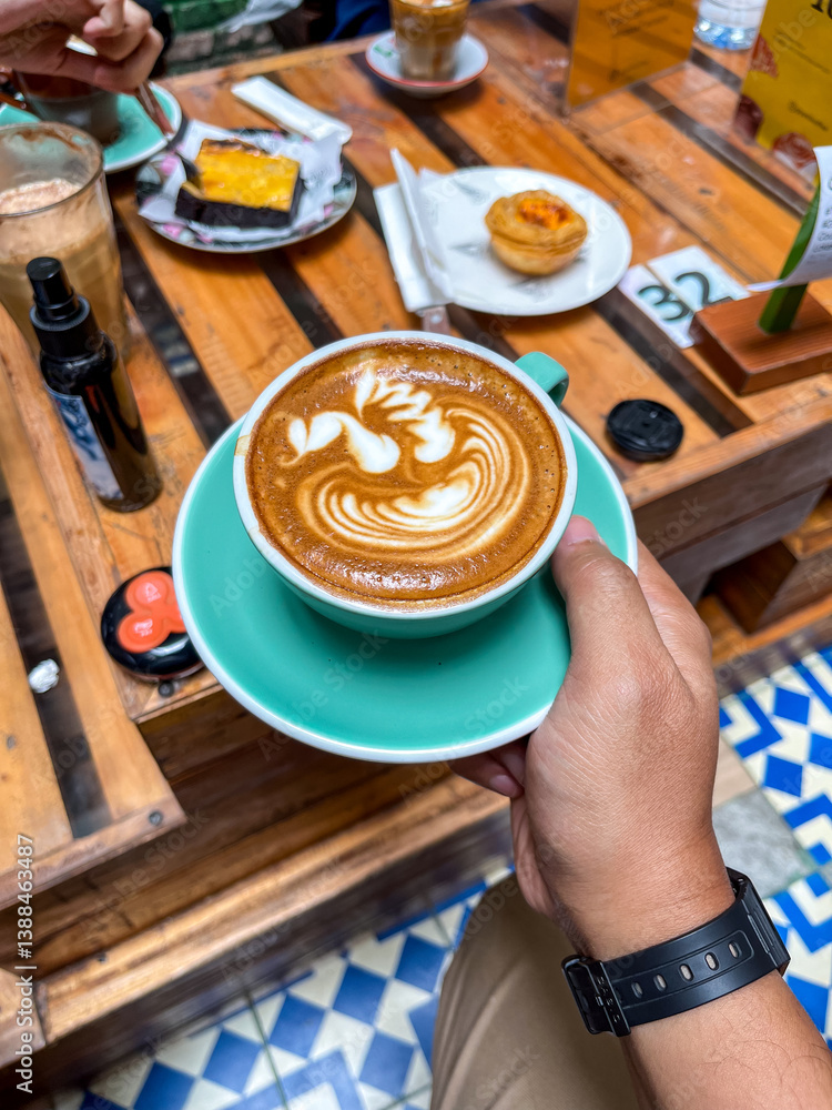 Magic Coffee with two ristretto shots and steamed milk served in a turquoise cup, held over a wooden table with pastries and drinks, capturing a cozy café moment.