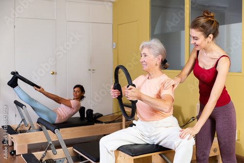 Obraz na płótnie Mature European woman who cares about her health is engaged in Pilates, performing an exercise with a special ring, where ..the coach helps to do it correctly w salonie