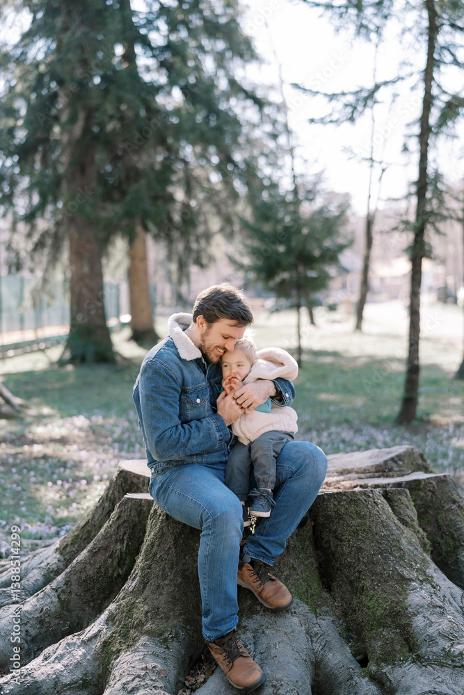 Smiling dad hugging a little girl sitting with her on a big stump in a sunny meadow Smiling dad hugging a little girl sitting with her on a big stump in a sunny meadow