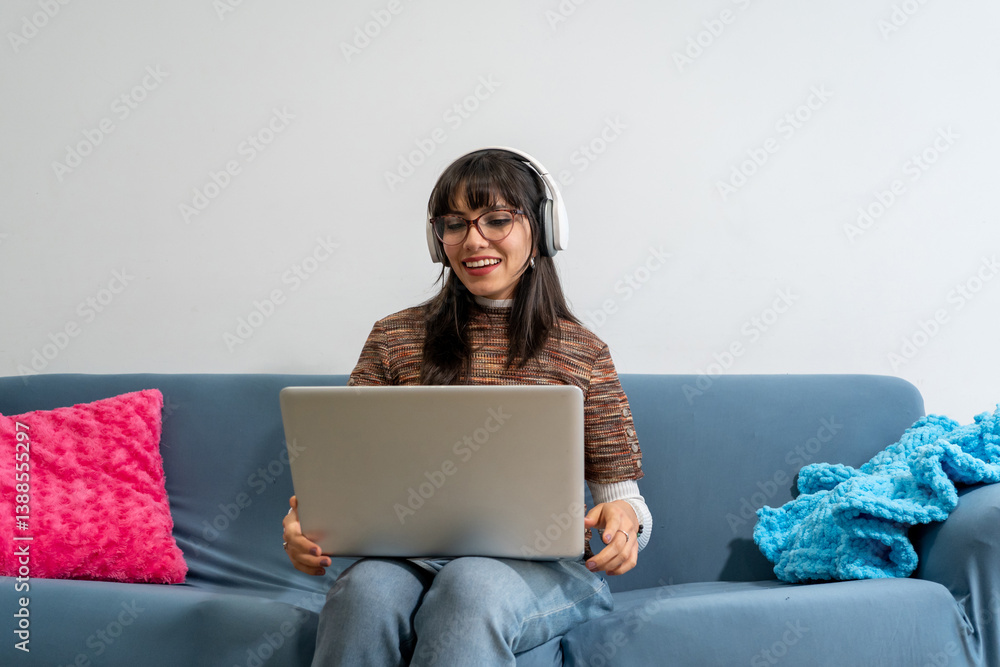 Young woman working from home using laptop and headphones on sofa Young woman working from home using laptop and headphones on sofa