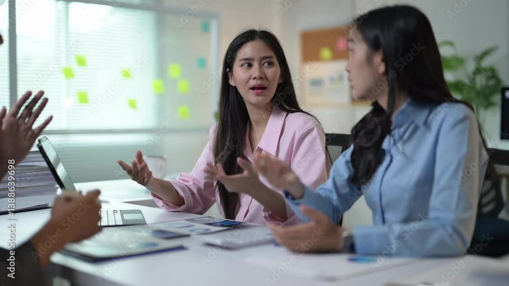 Three women are sitting at a table, talking to each other. One of the women is wearing a pink shirt Three women are sitting at a table, talking to each other. One of the women is wearing a pink shirt