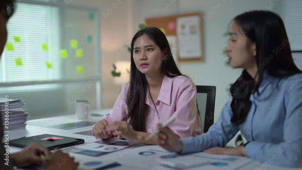Three women are sitting at a table, one of them is wearing a pink shirt. They are talking to each other and looking at some papers Three women are sitting at a table, one of them is wearing a pink shirt. They are talking to each other and looking at some papers