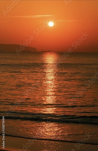 Obraz na płótnie Stunning sunset over the ocean with warm orange tones, calm waves, and silhouettes of distant ships