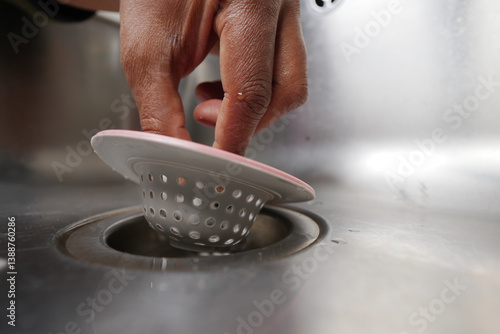 Slika na platnu Kitchen hand placing a sink strainer into a drain for cleanup