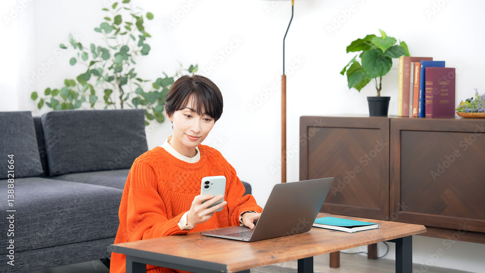 リビングルームでスマホとノートパソコンを使うミドル女性