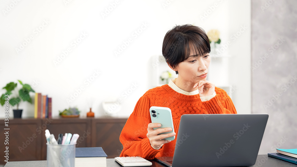 スマホとノートパソコンを見ながら悩むミドル女性
