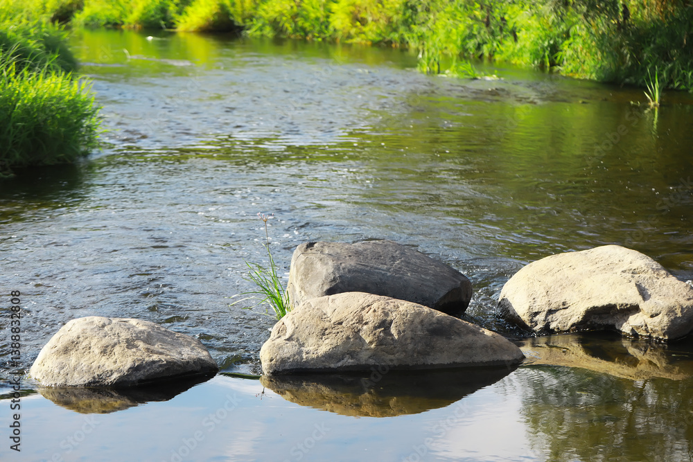 Fototapeta premium Tranquil River with Natural Rocks and Green Grassy Banks on a Sunny Day