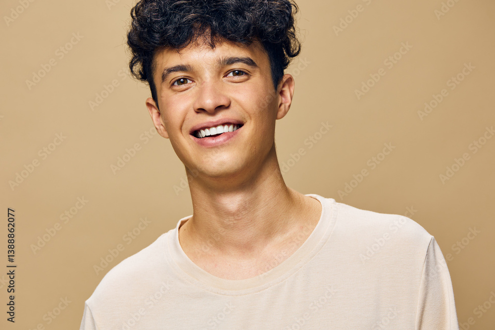 Smiling young man with curly hair wearing a light shirt, set against a warm, beige background that enhances the cheerful and friendly atmosphere of the portrait