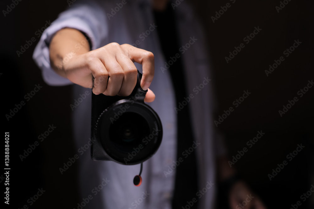 A tight shot of a person carefully holding a camera in front of a black backdrop, in a studio. A tight shot of a person carefully holding a camera in front of a black backdrop, in a studio.