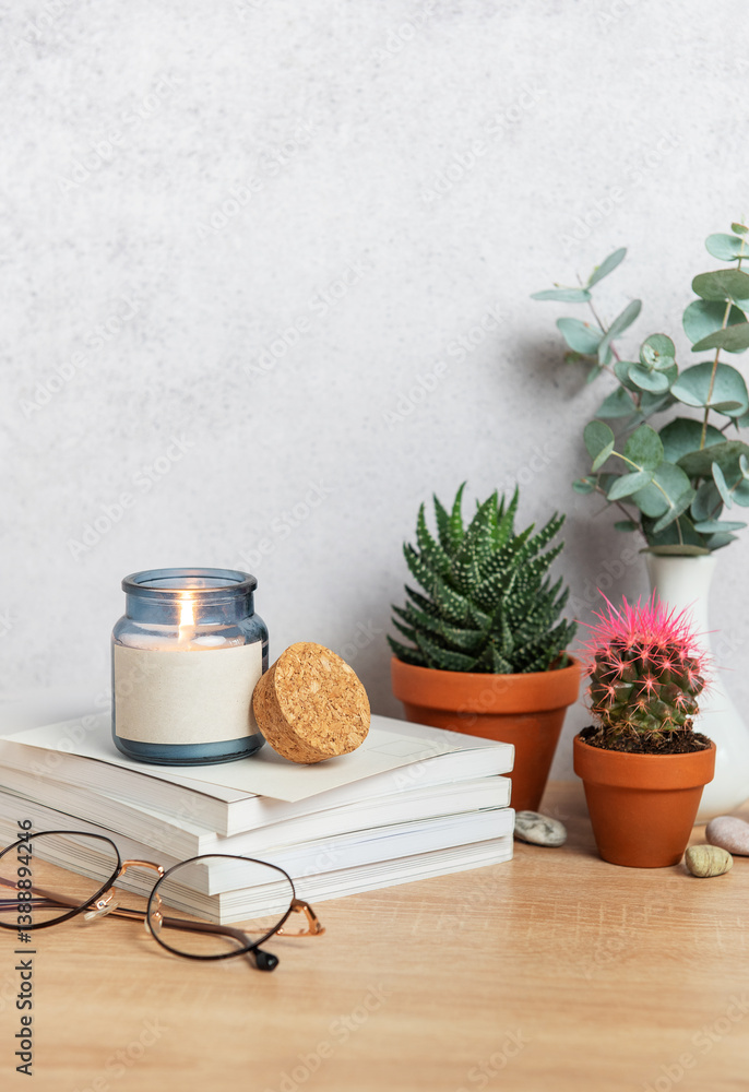Burning candle, books, eyeglasses, plants and vase creating cozy atmosphere on wooden desk