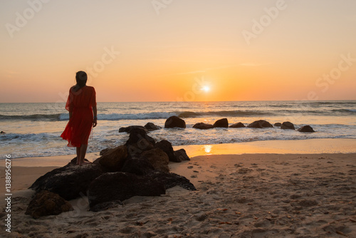 silhouette of a woman in red dress standing on rocks in the ocean on the beach at sunset