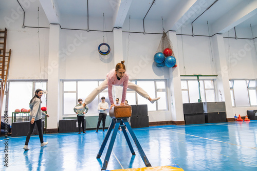 Schilderij op canvas Young gymnast practicing split leap over pommel horse during physical education