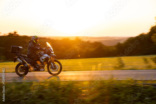 Driver riding motorcycle on empty road during sunset, spring mountains