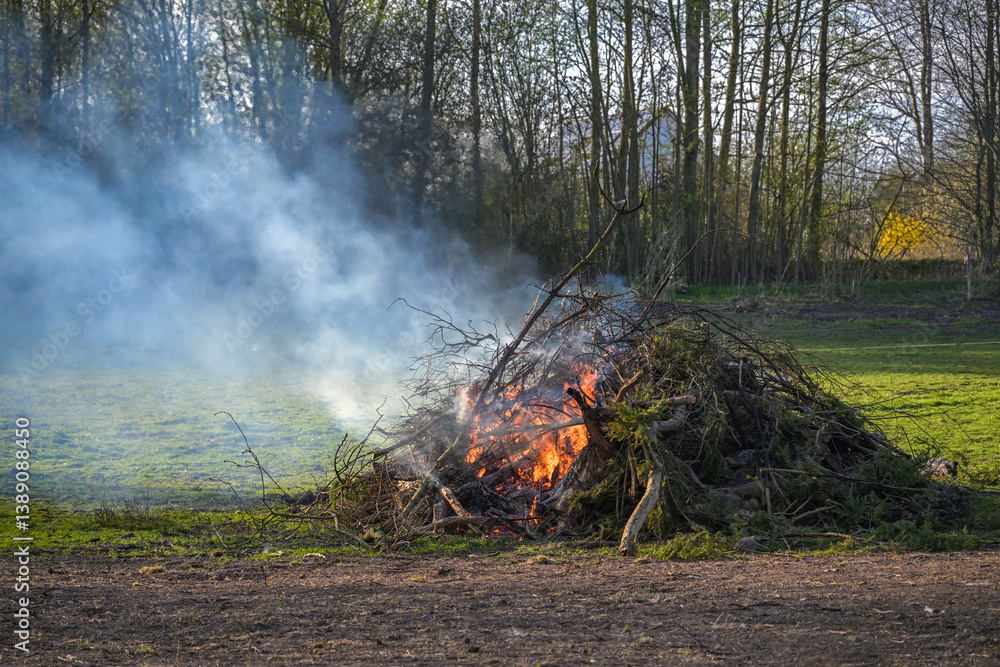 Large heap from branches, twigs and tree cuttings burning on a meadow, garden fire or traditional Easter fire, copy space