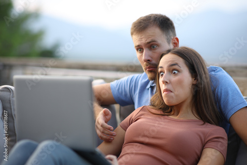 Photos Confused couple watching media content on laptop in a terrace