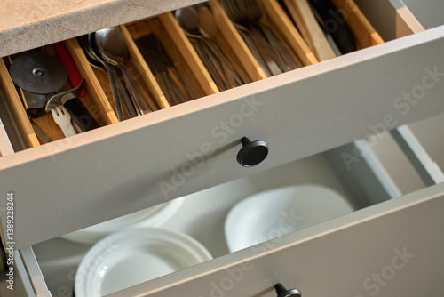 Modern kitchen with dishes and cutlery in open drawers. Contemporary kitchen cabinets. Concept of home organization and functionality interior