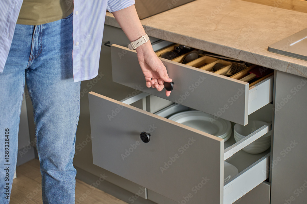Person opens a kitchen drawer with various utensils in wooden cutlery tray. Woman opening kitchen cabinet. Concept of home organization and functionality interior