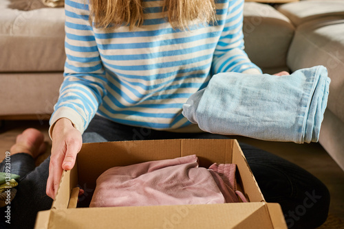 Obraz na płótnie Woman packs cardboard donation box with clothes in living room. Person preparing used clothing for recycling or second hand. Concept of charity, social care and volunteering w salonie
