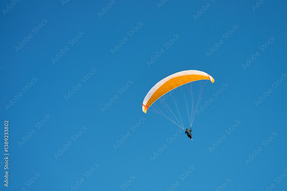Person is flying on paraglider against blue sky. Paraglide with yellow canopy. Extremal sport