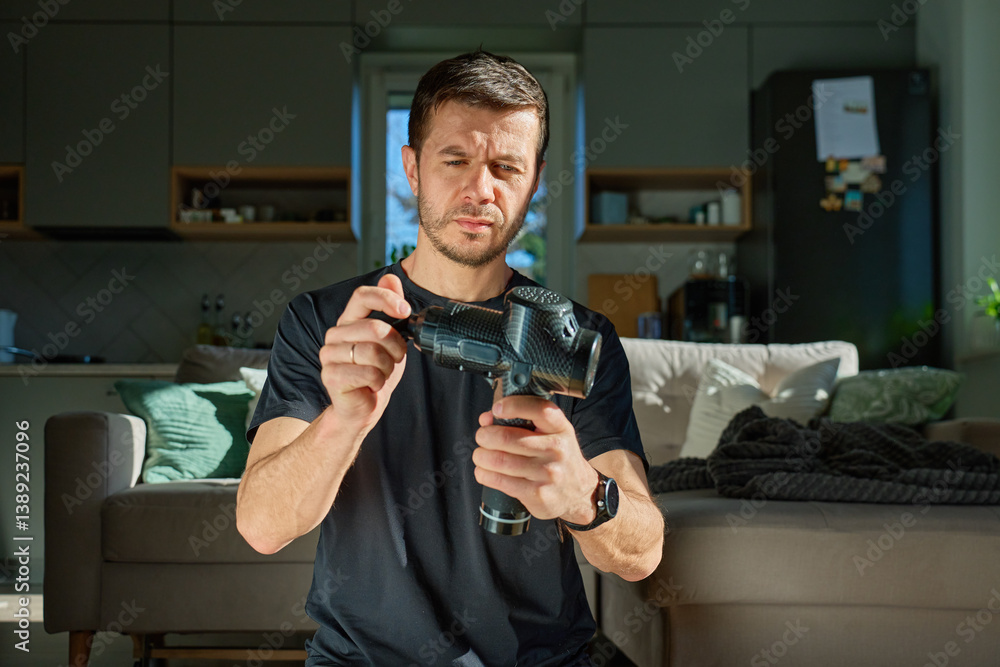 Close-up of man holding massage gun and pressing its vibrating head against his hand to test its strength and performance. Concept of sports recovery, self-care, and muscle treatment tools