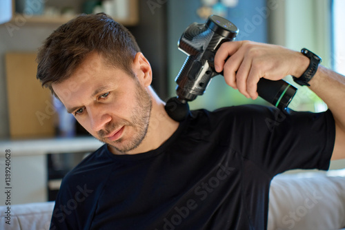 Obraz na płótnie Man applies massage gun to relieve tension in neck and shoulder area. Male athlete doing self-massage therapy with percussion device for recovery after training w salonie