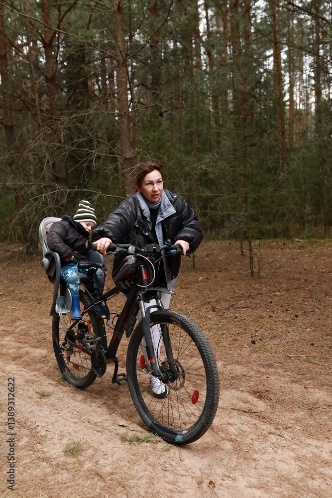 Mother rides bicycle through forest trail with child in seat enjoying outdoor adventure in winter season