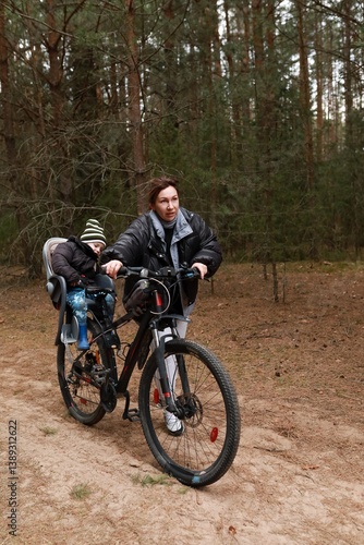 Obraz na płótnie Mother rides bicycle through forest trail with child in seat enjoying outdoor adventure in winter season w salonie