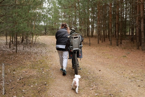 Obraz na płótnie Woman walks with child on bicycle in forest while dog runs alongside them during a sunny afternoon outing w salonie