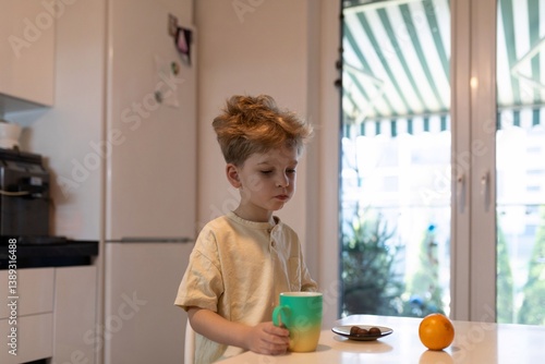 Child enjoying breakfast on a sunny morning in a cozy kitchen while holding a colorful cup