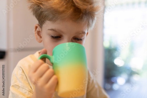 Obraz na płótnie Young child enjoys a colorful mug of beverage while sitting at home in daytime w salonie