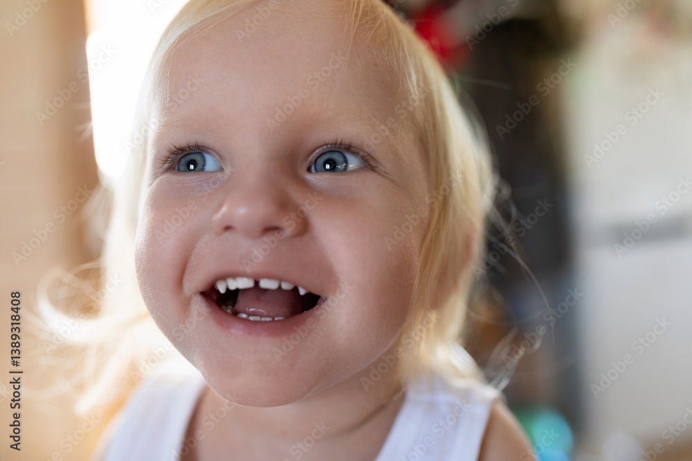 Cheerful child with bright blue eyes smiling joyfully in a cozy indoor setting during day time