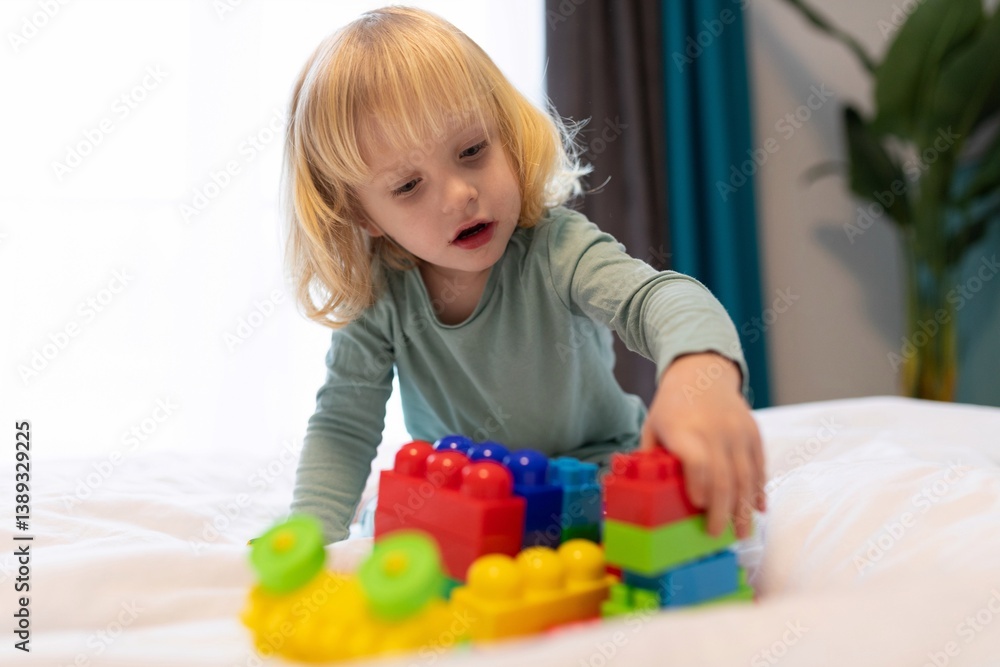 Child builds colorful structures with blocks on a bed in a cozy indoor setting during the afternoon