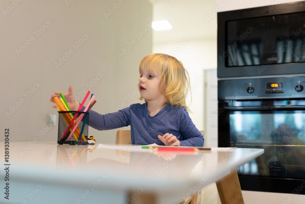 Child engages in creative drawing activity at a kitchen table with colorful markers in the morning light