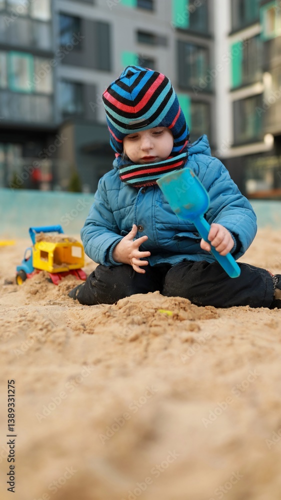 Child playing in sandbox with toys at urban playground during sunny day