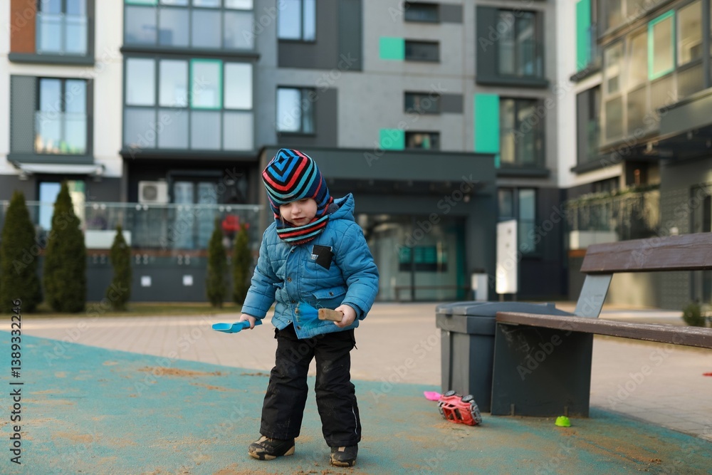 Child playing with toys on playground of modern residential building during winter afternoon