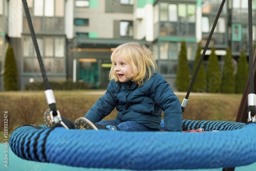 Obraz na płótnie Child enjoys swinging on a large tire swing in a modern park setting during the afternoon w salonie