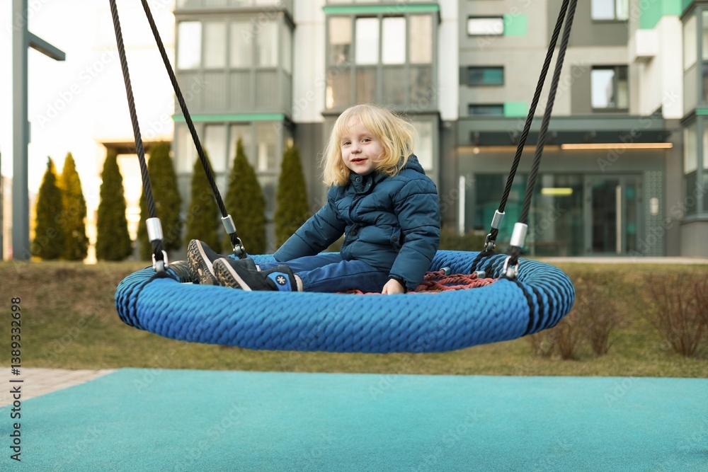 Child enjoys swinging on a circular swing in a modern playground during a sunny afternoon