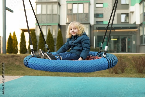 Obraz na płótnie Child enjoys swinging on a circular swing in a modern playground during a sunny afternoon w salonie