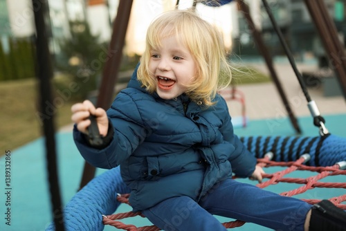 Obraz na płótnie Child joyfully playing on a swing set in a modern playground during a sunny afternoon in a city park w salonie