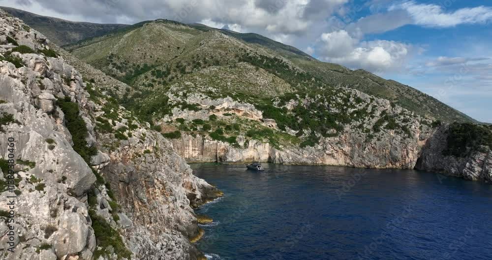 rocky cliffs and a grey yacht during the day with turquoise water in Shpella e Pellumbave, Albania, establishing aerial drone shot rocky cliffs and a grey yacht during the day with turquoise water in Shpella e Pellumbave, Albania, establishing aerial drone shot